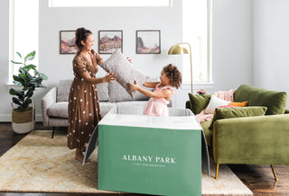 little girl popping out of an Albany Park box handing adult a pillow